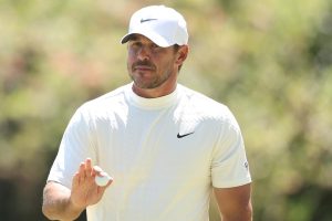Golfer in a white Nike cap and shirt holds a golf ball, preparing to throw or inspect it on a sunny course.