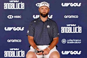 Man seated in front of a blue backdrop with 'Live Golf Andalusia' sponsor logos, wearing a navy polka-dot polo, white cap, and white shorts.