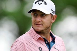 Male golfer wearing a pink striped polo and a white Callaway cap, looking to the side.