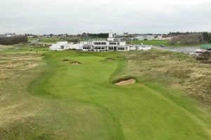 Green golf fairway with multiple sand bunkers leading to a white clubhouse in the distance.